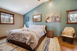 Ein Schlafzimmer mit Bett, Sessel, Nachttisch, Spiegel und Wandbildern.