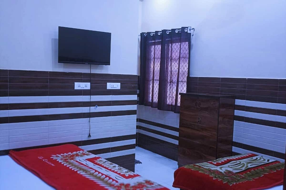 Habitación de hotel con dos camas, un televisor de pantalla plana, aire acondicionado y una ventana con cortina.