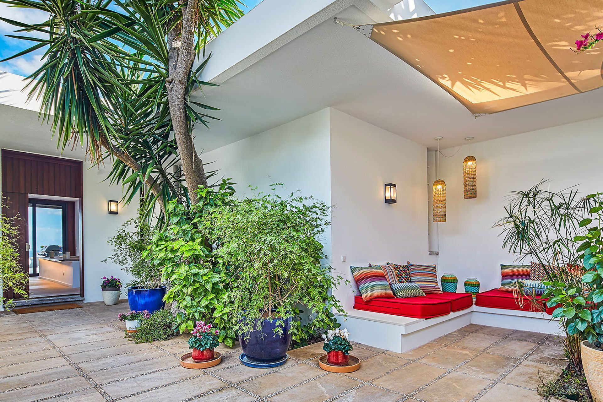 Un área de estar moderna al aire libre con plantas en macetas, una palmera y una pared blanca con dos luces empotradas.