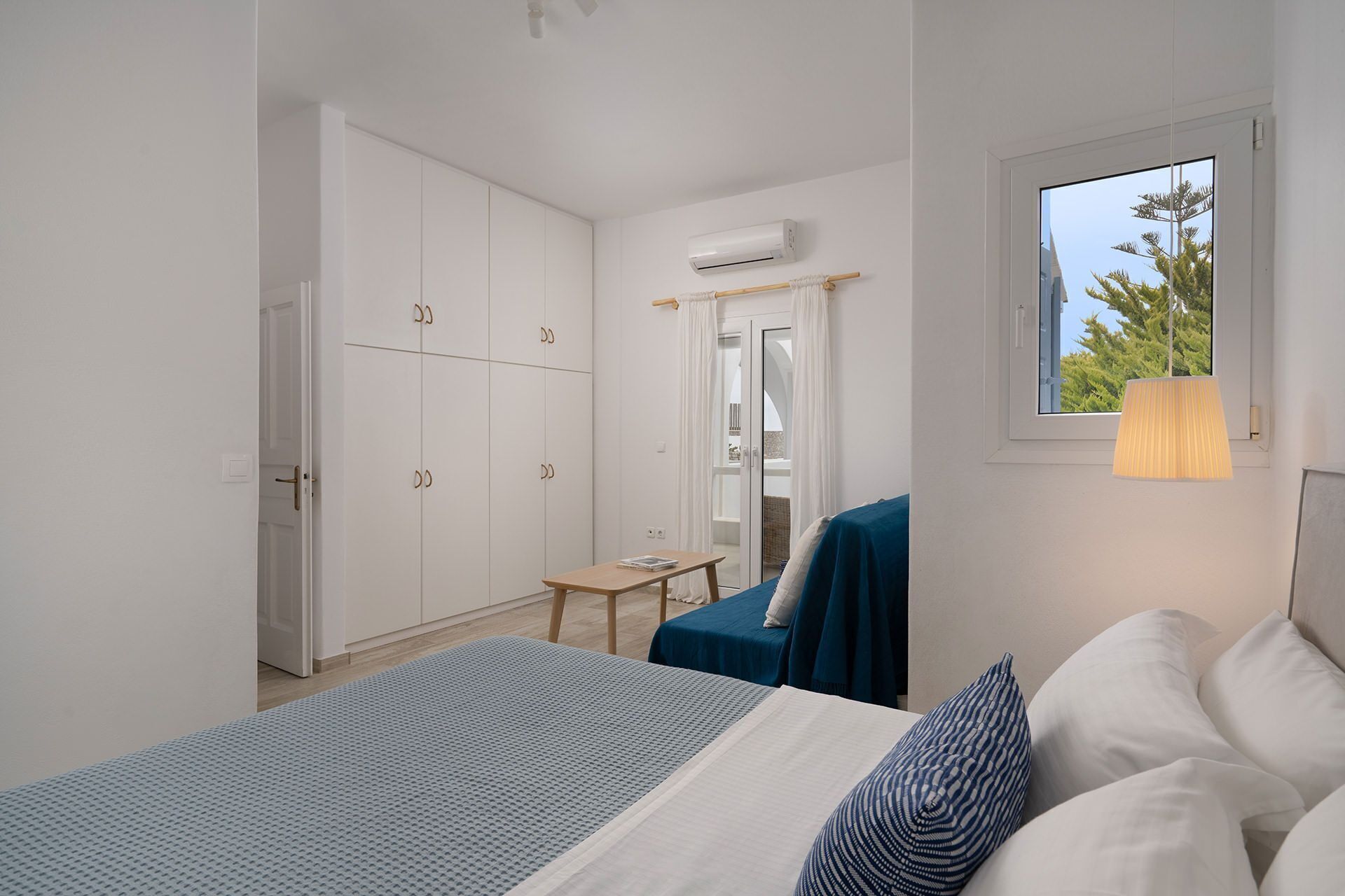 A bedroom with a bed, a desk, a wardrobe, and a window with a view.