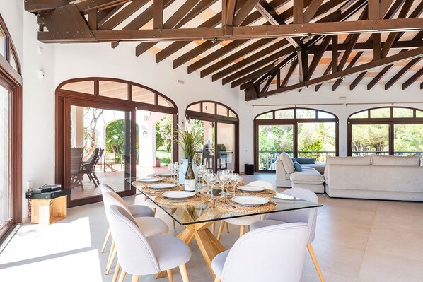 Un comedor espacioso con una mesa de vidrio, sillas blancas y vistas al exterior a través de amplios ventanales.