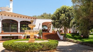 Un patio con una fuente, un edificio blanco con arcos y una escalera que lleva a una zona cubierta.