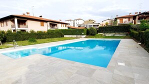 A rectangular swimming pool with a tiled deck, surrounded by a well-maintained lawn and hedges. - Apartment MoKi in Moniga del Garda (Moniga del Garda)