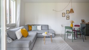 A modern living room with a grey sectional sofa, a small round coffee table, and a dining area with a table and chairs. - Apartment MoKi in Moniga del Garda (Moniga del Garda)