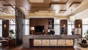 A reception area with a wooden reception desk, a TV, and a decorative wall with geometric patterns. - SSAW Boutique Hotel DeXin - Near Mount Mogan (Huzhou)