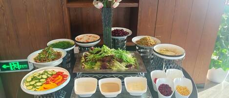 Un tavolo da buffet con diversi piatti, tra cui insalate, verdure e salse, disposti su un tavolo rotondo con uno sfondo in legno.