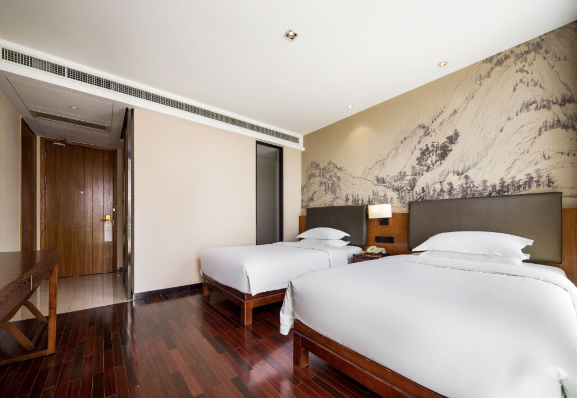 A hotel room with two beds, a wooden floor, a large wall mural, and a door leading to another room.
