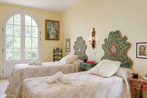 A room with two beds, a large arched window, and a painting on the wall.