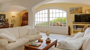 Una sala de estar con un sofá blanco, una mesa de centro y un ventanal con vistas a zonas verdes.