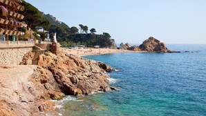 Un hotel costero con fachada de piedra, una escalera que lleva a la playa y vistas al mar y afloramientos rocosos.