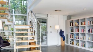 A modern interior with a wooden staircase, a black leather chair, a bookshelf, and a lamp. - My Rental Homes | Villa Luminosa with private pool and garden (Palafrugell)