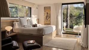 A modern bedroom with a large bed, a bedside table with a lamp, a chair, and a view of the outdoors.