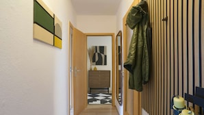 Ein Flur mit Holzboden, einer Holztür und einem an der Wand befestigten Garderobenhaken mit Jacken.