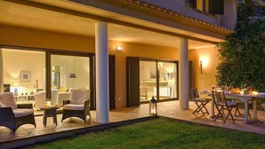 Un área de patio al aire libre con asientos y una mesa de comedor, rodeada de grandes ventanales y puertas que dan a espacios interiores.