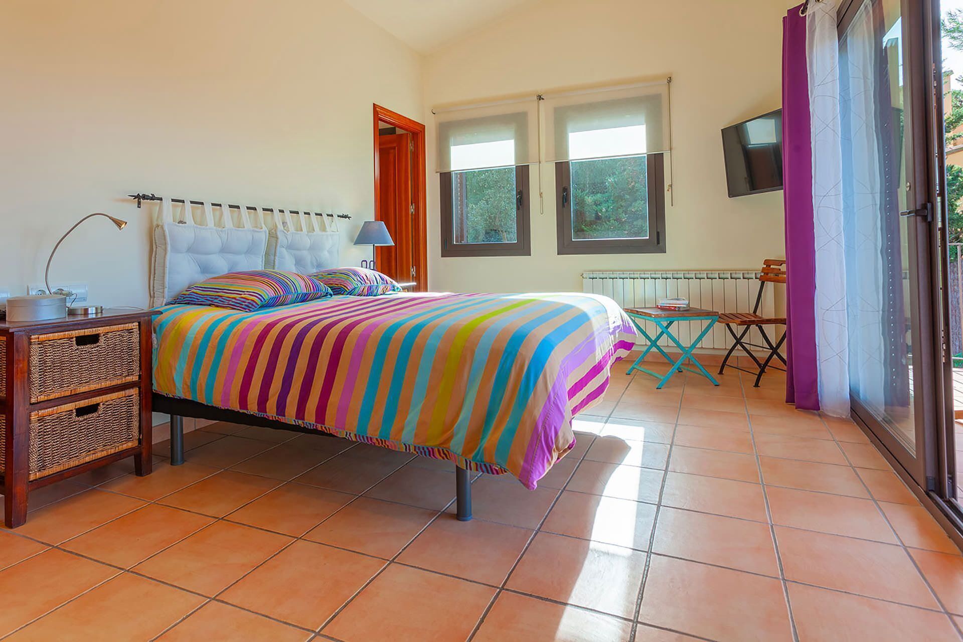 Une chambre à coucher avec un lit, une table de chevet, une lampe et une fenêtre avec des rideaux.