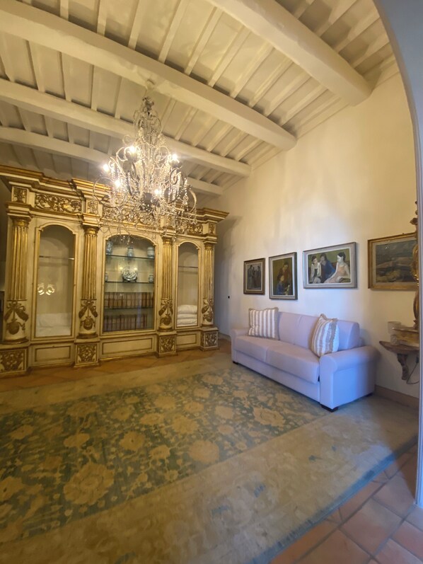 A room with a patterned floor, a white sofa, a chandelier, and a decorative cabinet with glass doors.