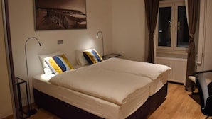 Une chambre à coucher avec un grand lit, deux tables de chevet, une commode, une fenêtre avec des rideaux et une œuvre d’art accrochée au mur.