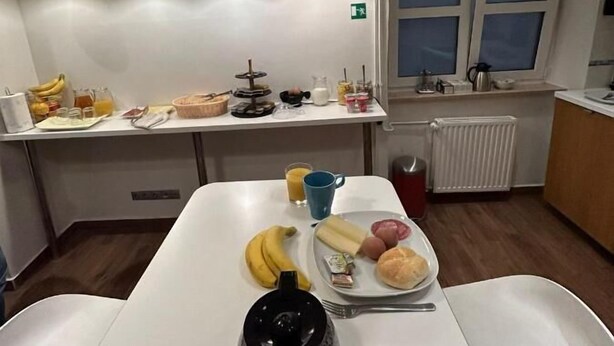 Une cuisine moderne avec un plan de travail blanc, une bouilloire et un assortiment de produits pour le petit-déjeuner comprenant des bananes, des œufs et du pain.