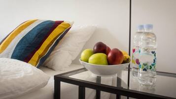 A white couch with a striped pillow, a bowl of fruit, and two water bottles on a glass table.