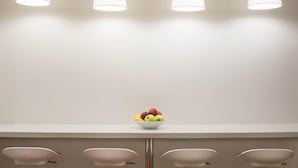 Un comptoir blanc avec quatre tabourets et un saladier de fruits posé dessus.
