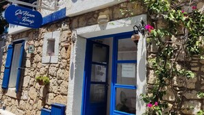 A traditional stone building with a blue door and windows, a signboard, and potted plants. - Gül Hanım Konağı (Cesme)