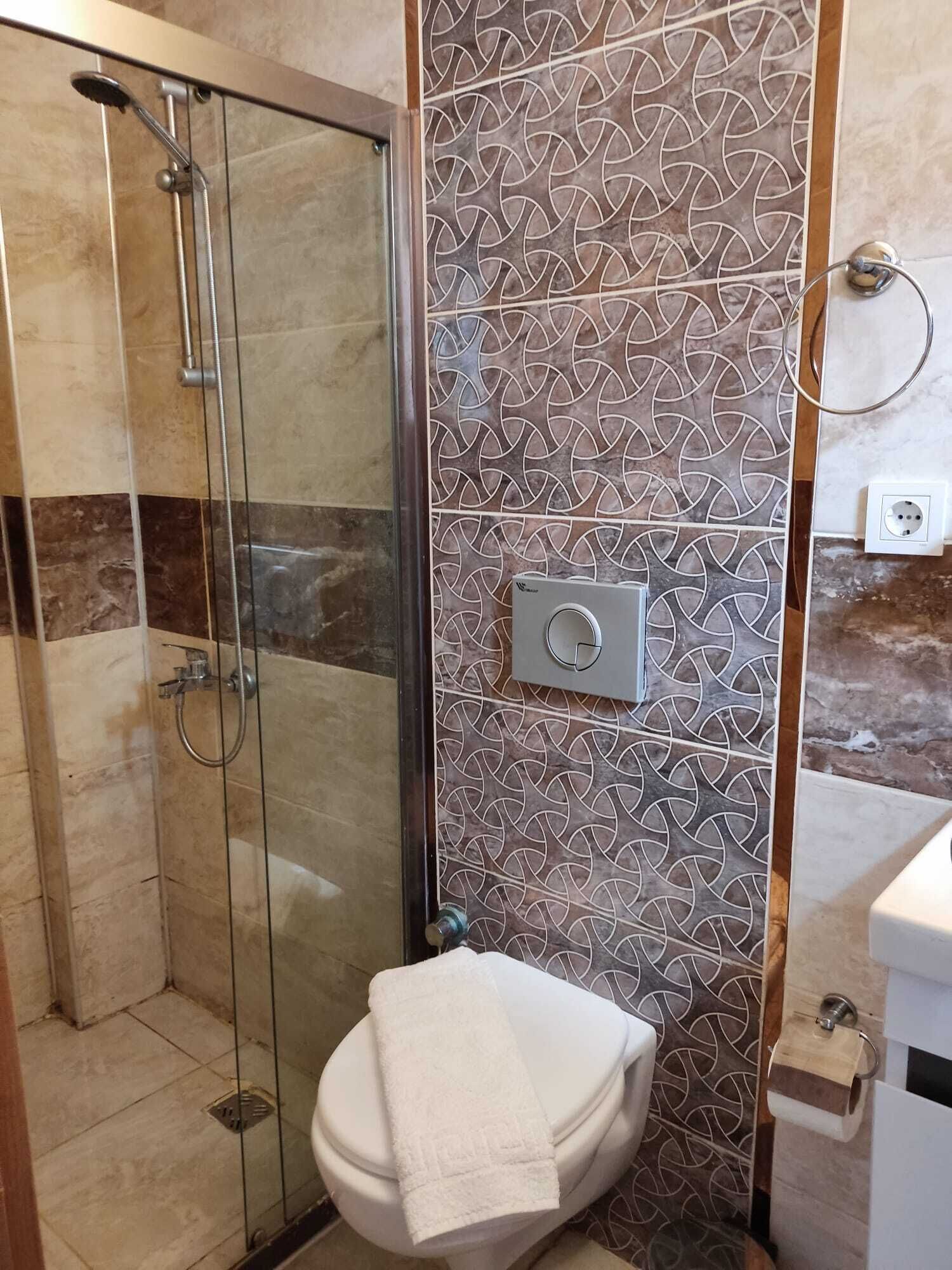 Casa de banho com cabine de chuveiro em vidro, sanita e dispensador de toalhas fixado na parede.