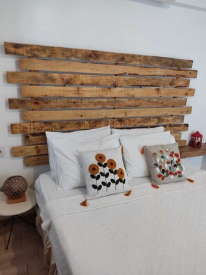 A bed with white bedding, two decorative pillows with floral designs, and a wooden slat headboard.
