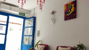 A room with two plush armchairs, a wall-mounted painting, a ceiling with hanging pink flowers, and a door with an exit sign. - Gül Hanım Konağı (Cesme)