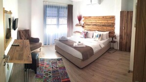 A modern hotel room with a large bed, a wooden headboard, a desk with a chair, a small table, and a colorful rug. - Gül Hanım Konağı (Cesme)