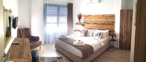 A modern hotel room with a large bed, a wooden headboard, a desk with a chair, a small table, and a colorful rug.