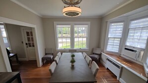 A dining room with a large table, chairs, a chandelier, and large windows with blinds. - Historic Mayor`s Manor | 2 King Bds • Fenced Yard (Sanford)
