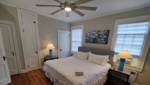 A bedroom with a large bed, two bedside tables, a ceiling fan, and a window with blinds. - Historic Mayor`s Manor | 2 King Bds • Fenced Yard (Sanford)