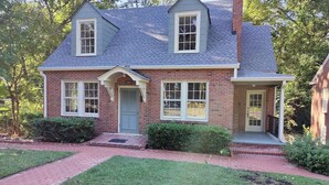A two-story brick house with a grey roof, a front porch, and a well-maintained lawn. - Historic Mayor`s Manor | 2 King Bds • Fenced Yard (Sanford)