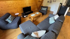 A cozy log cabin interior with a wooden ceiling, a television on a stand, grey sofas, and a small table with a remote control. - L'Echappée Verte, your nature cocoon in the heart of Alsace Verte (Dambach)