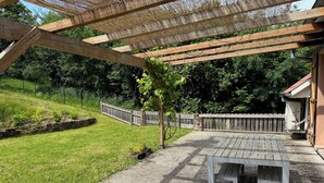 A covered patio area with a wooden table and benches, surrounded by a stone wall and a wooden fence. - L'Echappée Verte, your nature cocoon in the heart of Alsace Verte (Dambach)