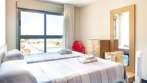 Habitació d'hotel amb dos llits, una cadira vermella, un taulell, un mirall i una finestra amb vista a la ciutat.