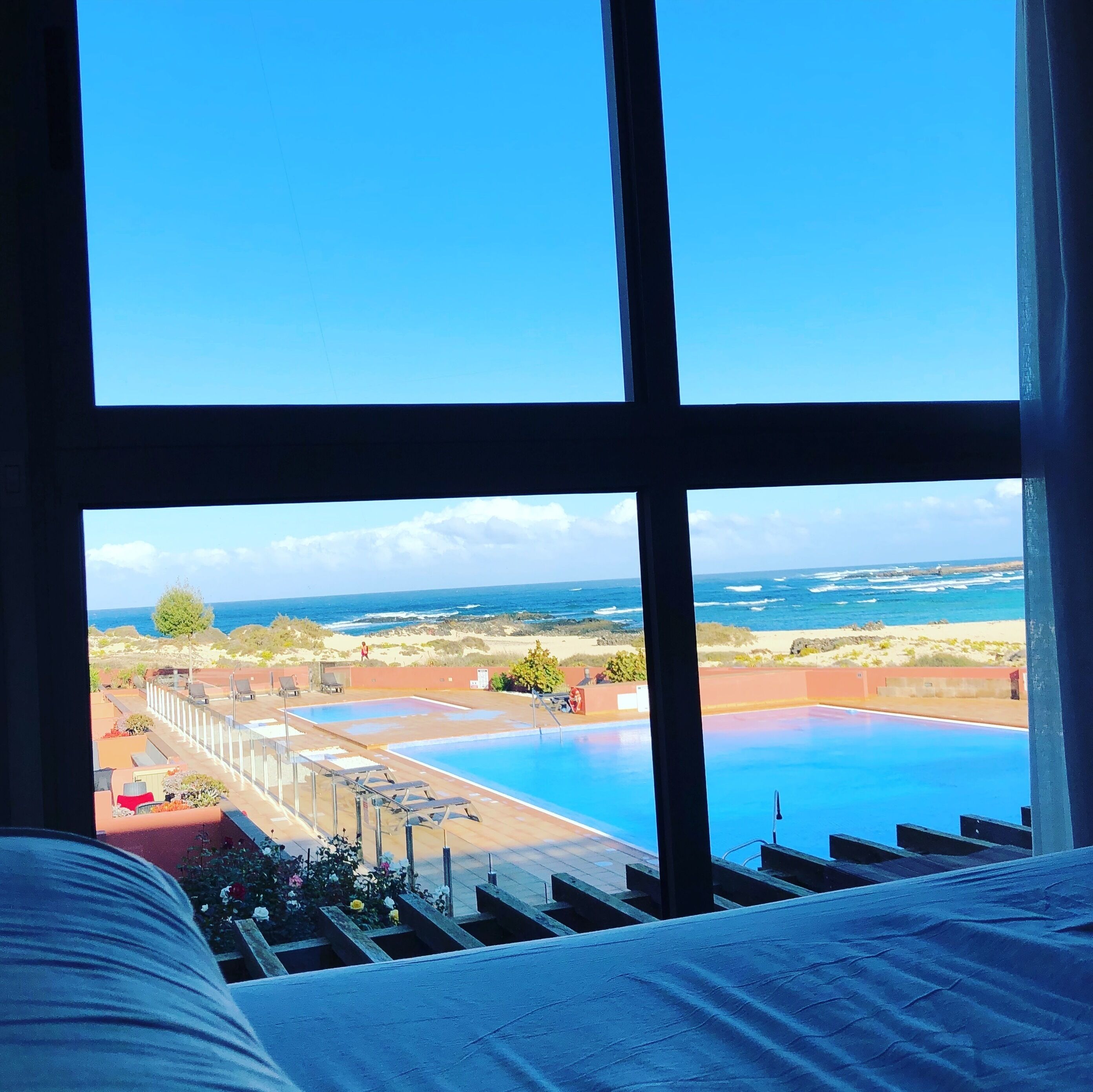 Ein Hotelzimmer mit großem Fenster und Blick auf Pool und Strand.