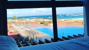 Habitació d'hotel amb una finestra gran que dona a una piscina i una platja.