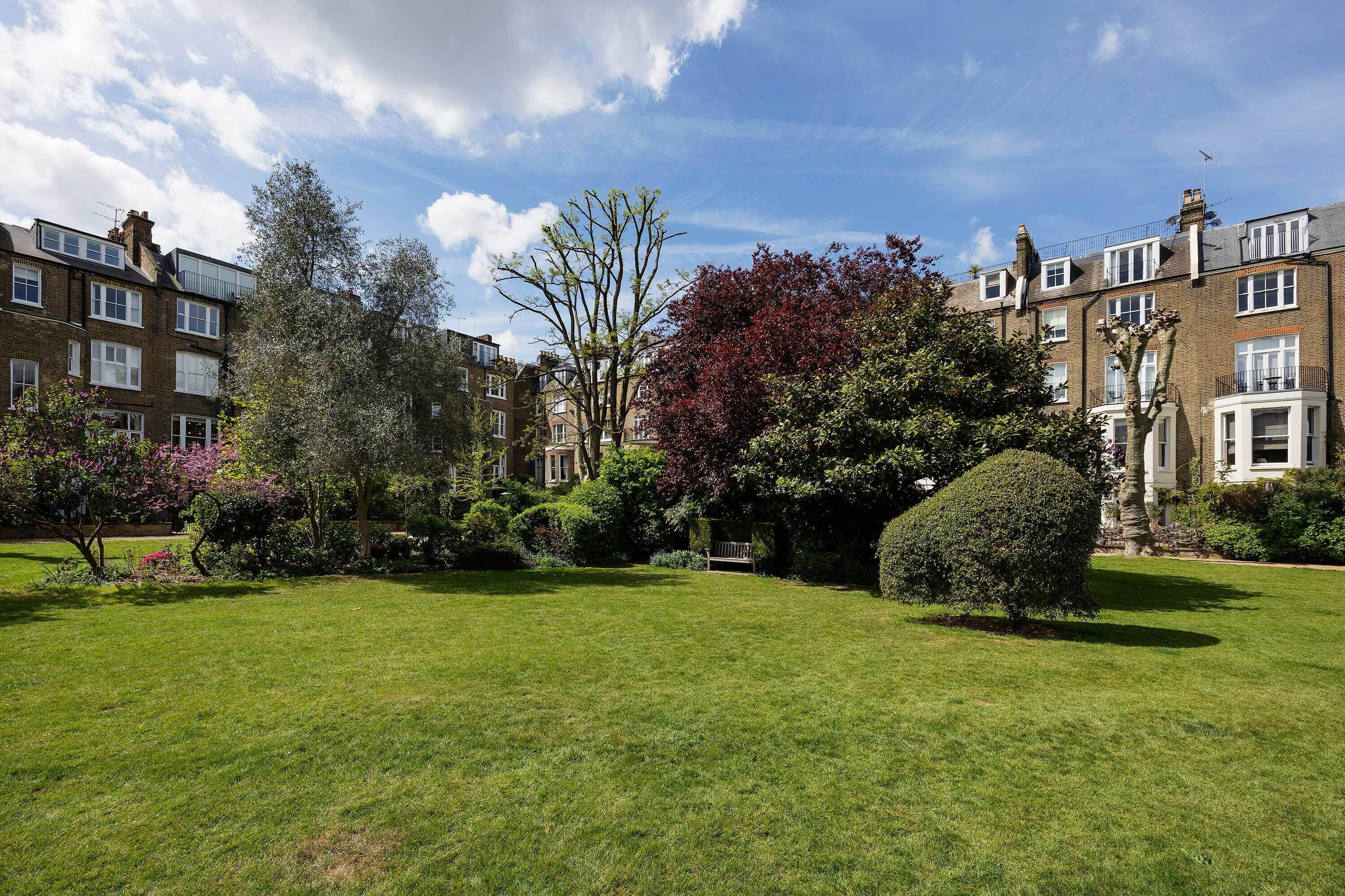 A well-maintained garden with a lawn, mature trees, and a bench.