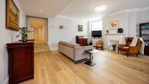 A living room with a sofa, a coffee table, a fireplace, and a wooden floor. - The Maida Vale Garden Apartment, by Veeve (London)