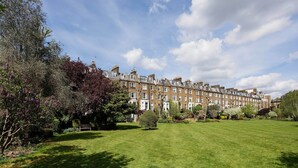 A row of terraced houses with a well-maintained lawn in front. - The Maida Vale Garden Apartment, by Veeve (London)
