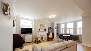A spacious living room with a beige sofa, a TV, and a fireplace. - The Maida Vale Garden Apartment, by Veeve (London)