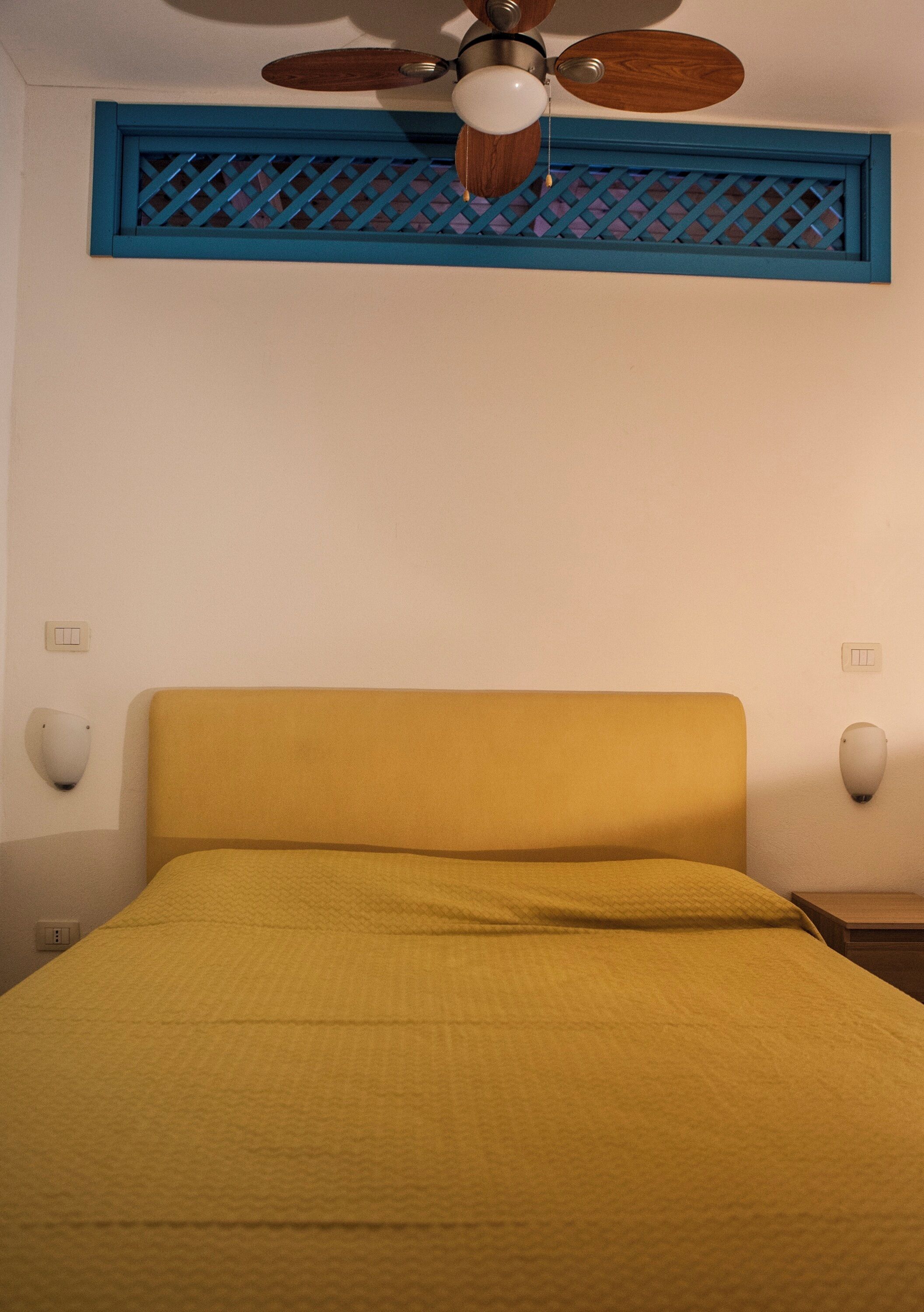 Une chambre avec un lit, un ventilateur de plafond et des appliques murales.