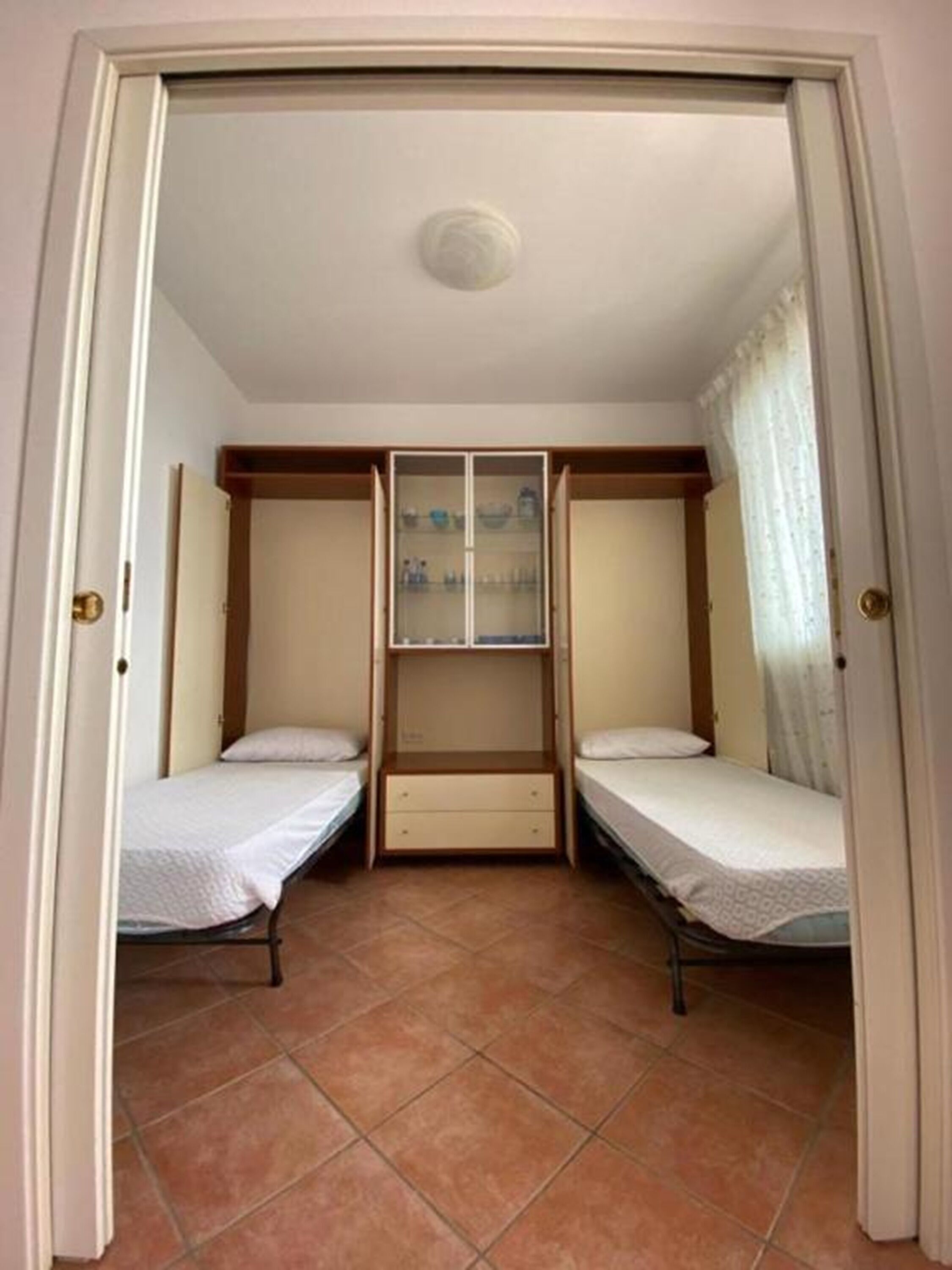Une chambre avec deux lits simples, une armoire en bois et un meuble vitré avec des étagères.