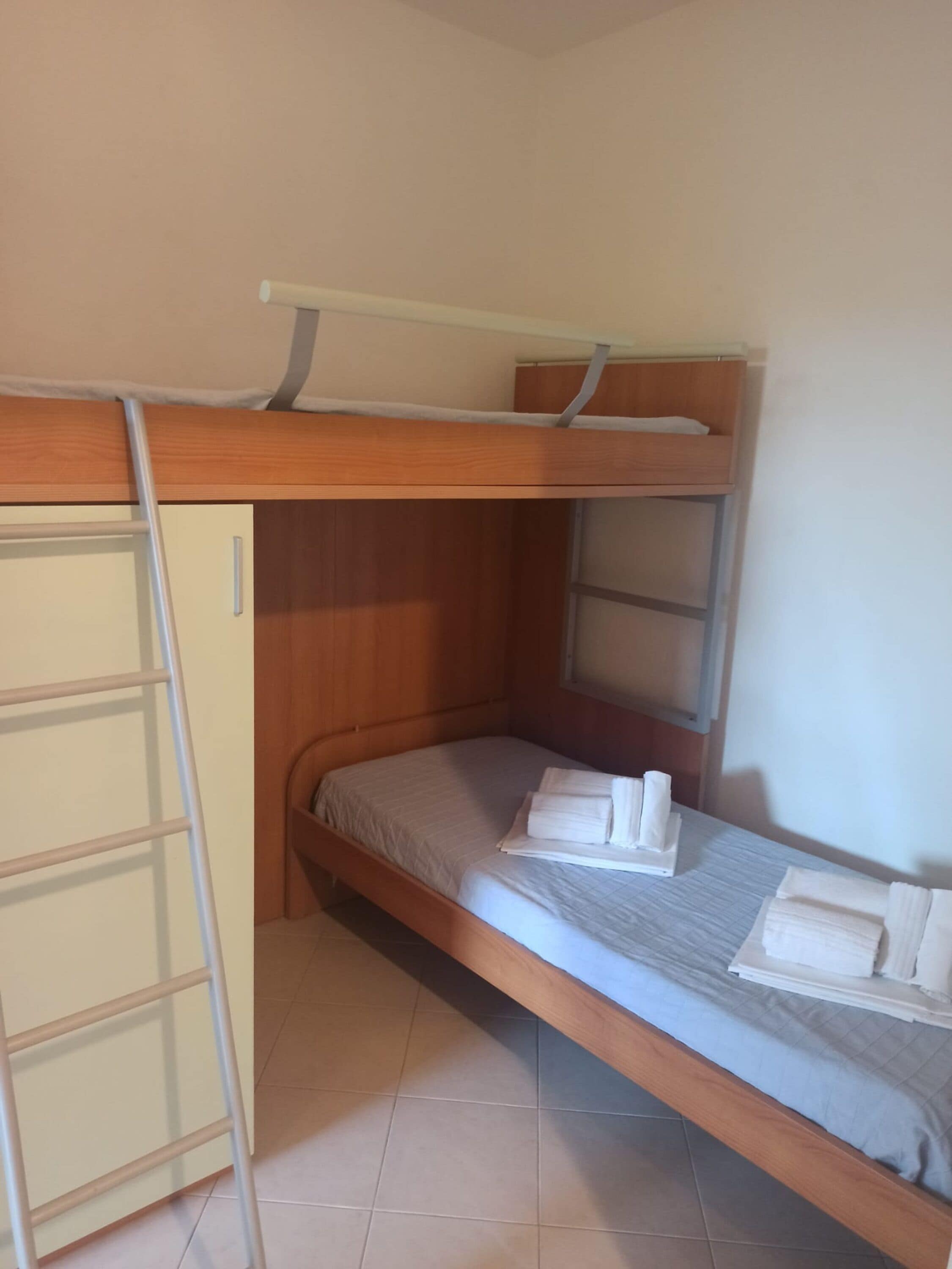 Un lit superposé avec une échelle, une petite armoire en bois et des serviettes soigneusement pliées sur le lit.