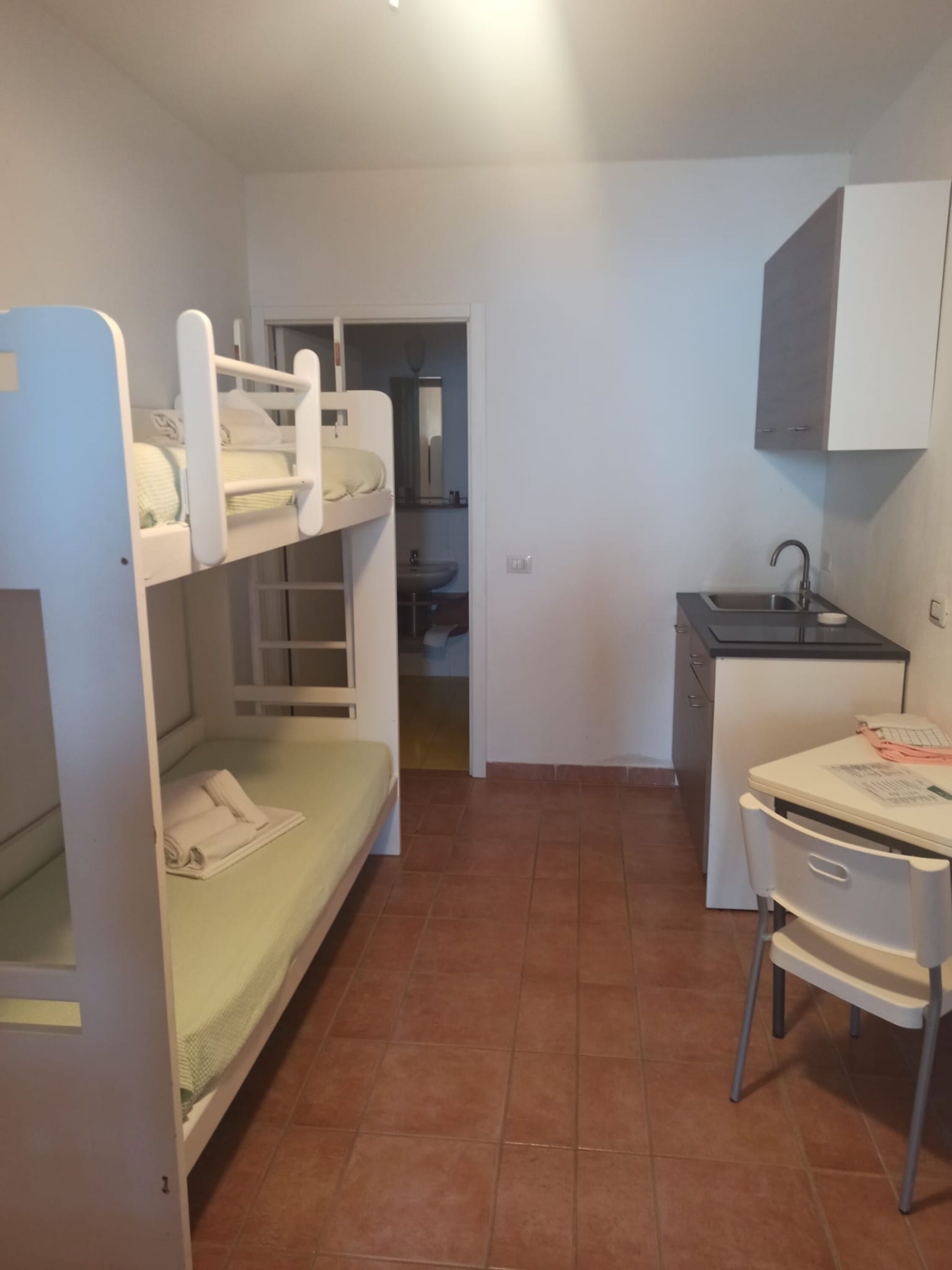 Een kleine kamer met stapelbedden, een kitchenette en één stoel.