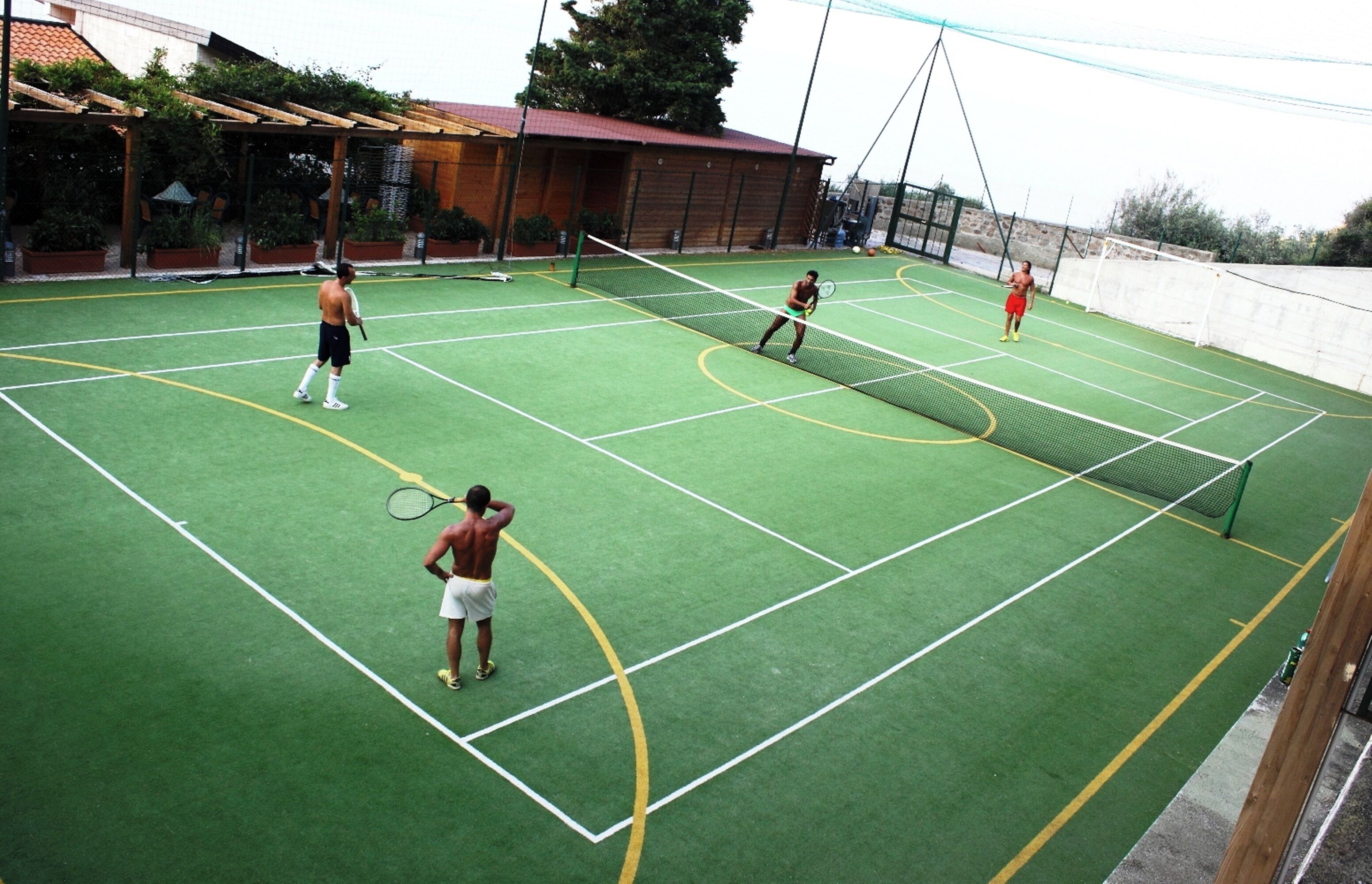 En indendørs tennisbane med net, grøn gulvbelægning og et træværn hele vejen rundt.