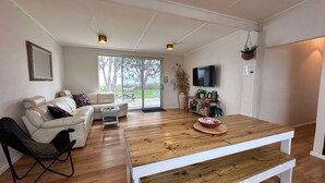 A spacious living room with a wooden floor, a white sofa, a black chair, a coffee table, and a TV mounted on the wall.