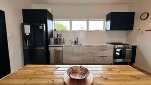 A modern kitchen with a black refrigerator, microwave, dishwasher, and stove. There is a wooden table with a bowl in the center.