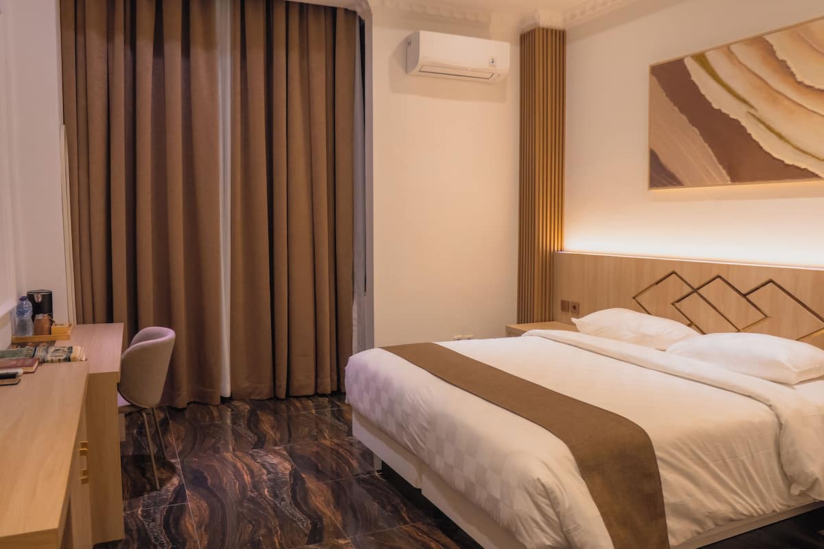 Habitación de hotel con cama, escritorio, silla y ventana grande con cortinas.
